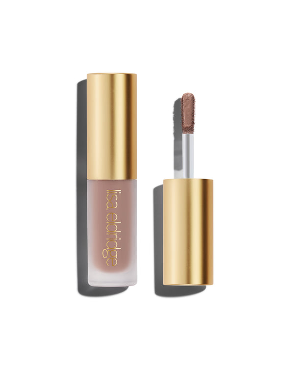 A closed bottle of Lisa Eldridge Liquid Silk Liquid Eyeshadow in cool mauve shade Ione, with a gold cap containing an applicator wand with product on it, against a white background.